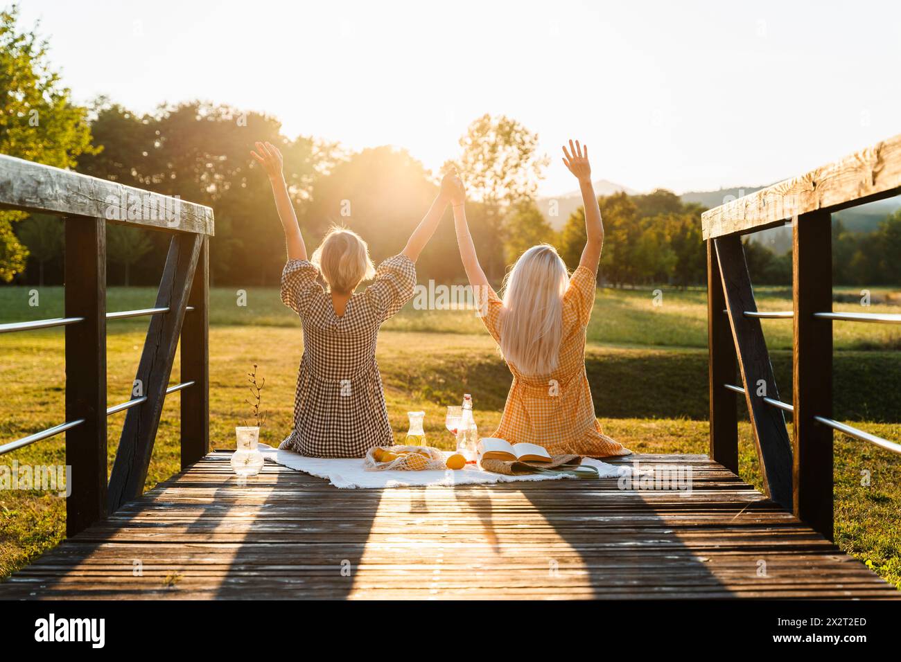 Friends with arms raised sitting on boardwalk in park Stock Photo