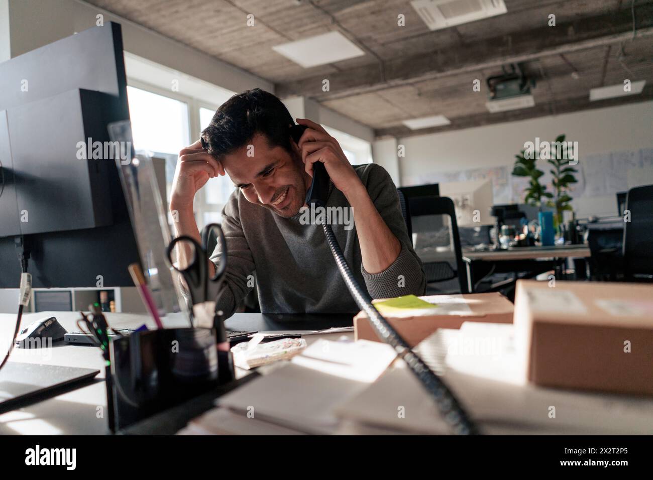 Happy businessman talking on landline phone at desk in office Stock Photo