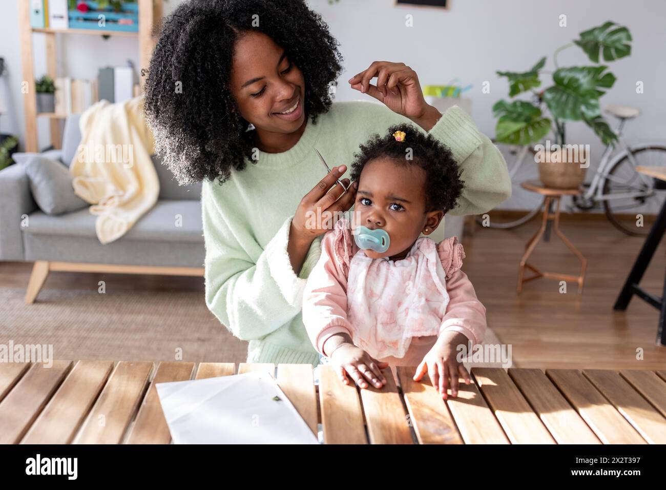 Smiling single mother with scissors cutting hair of baby girl at home Stock Photo