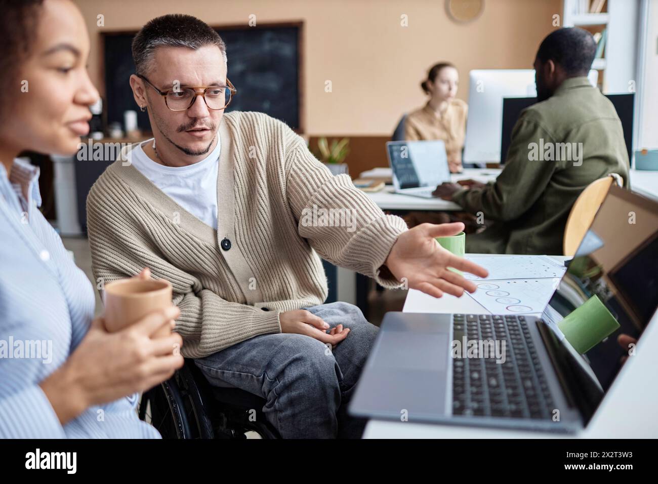 Businessman with disability having discussion over new computer software on laptop with businesswoman at desk Stock Photo
