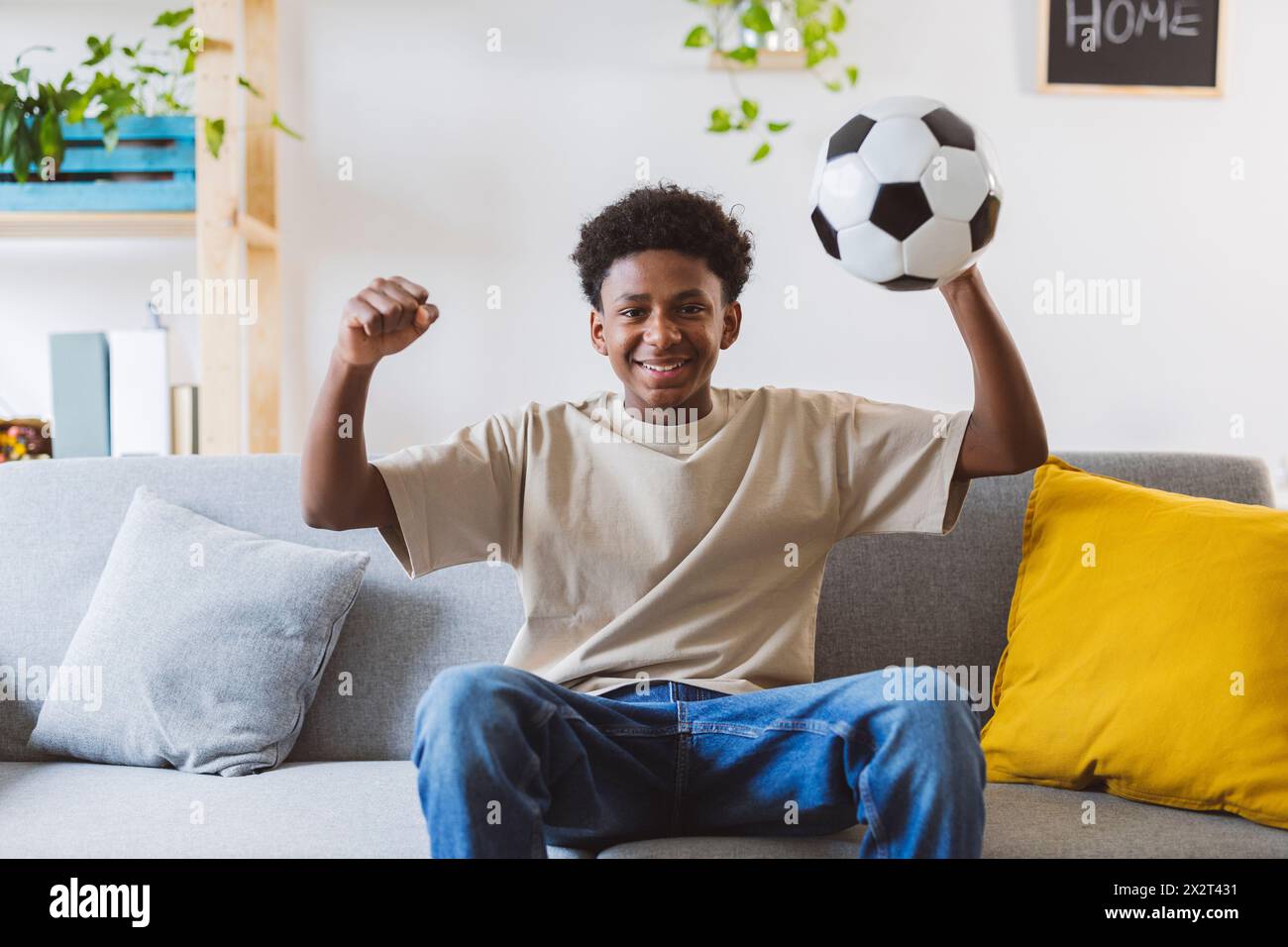 Cheerful boy holding soccer ball watching match at home Stock Photo
