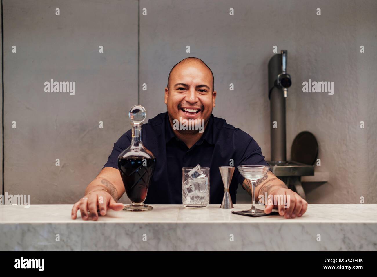 Smiling bartender with cocktail and alcohol bottle at bar counter in restaurant Stock Photo