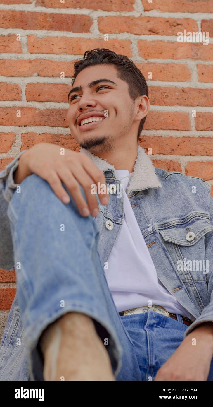 Smiling young man sitting near brick wall Stock Photo