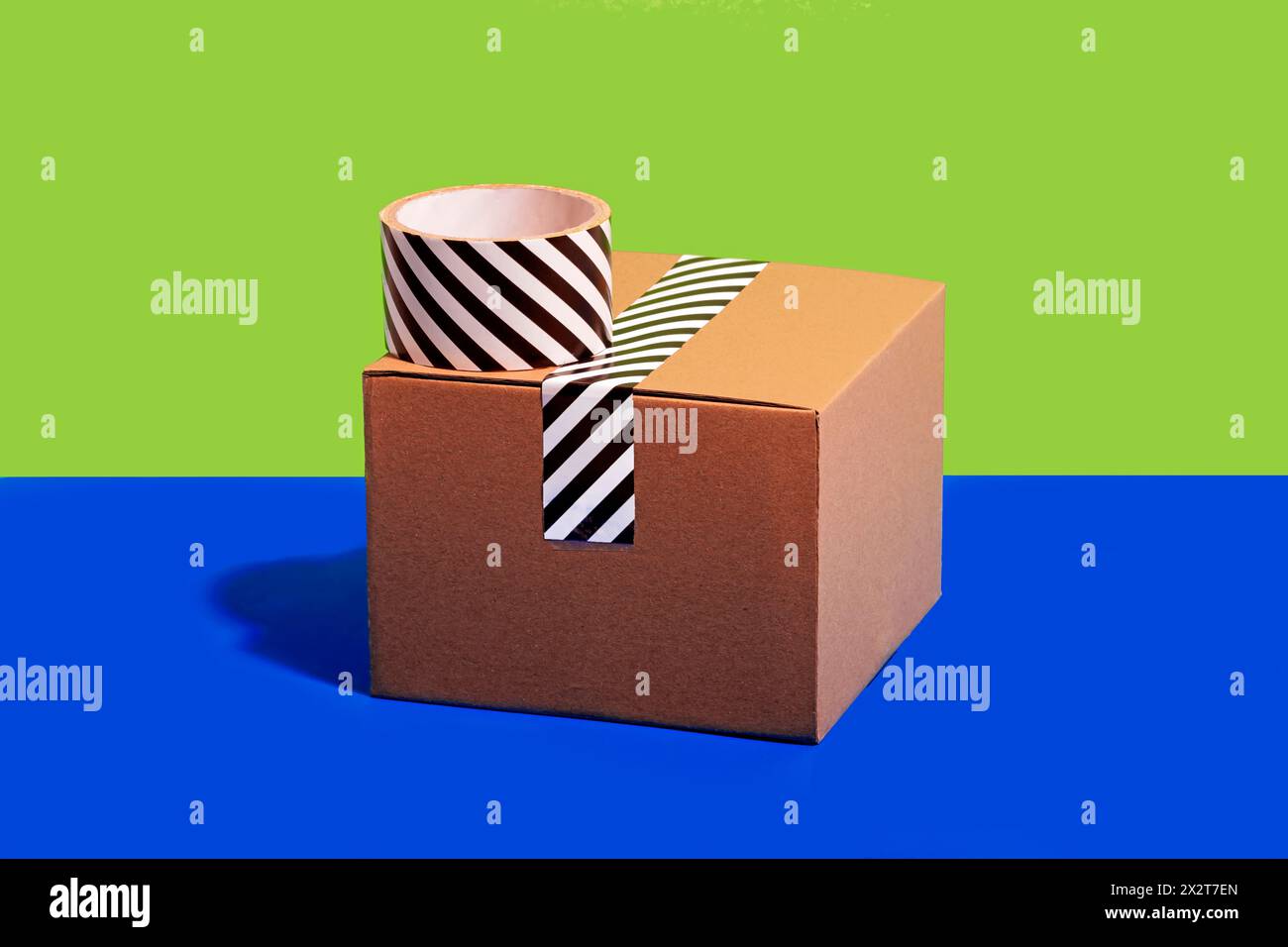 Striped adhesive tape and cardboard box against green and blue background Stock Photo