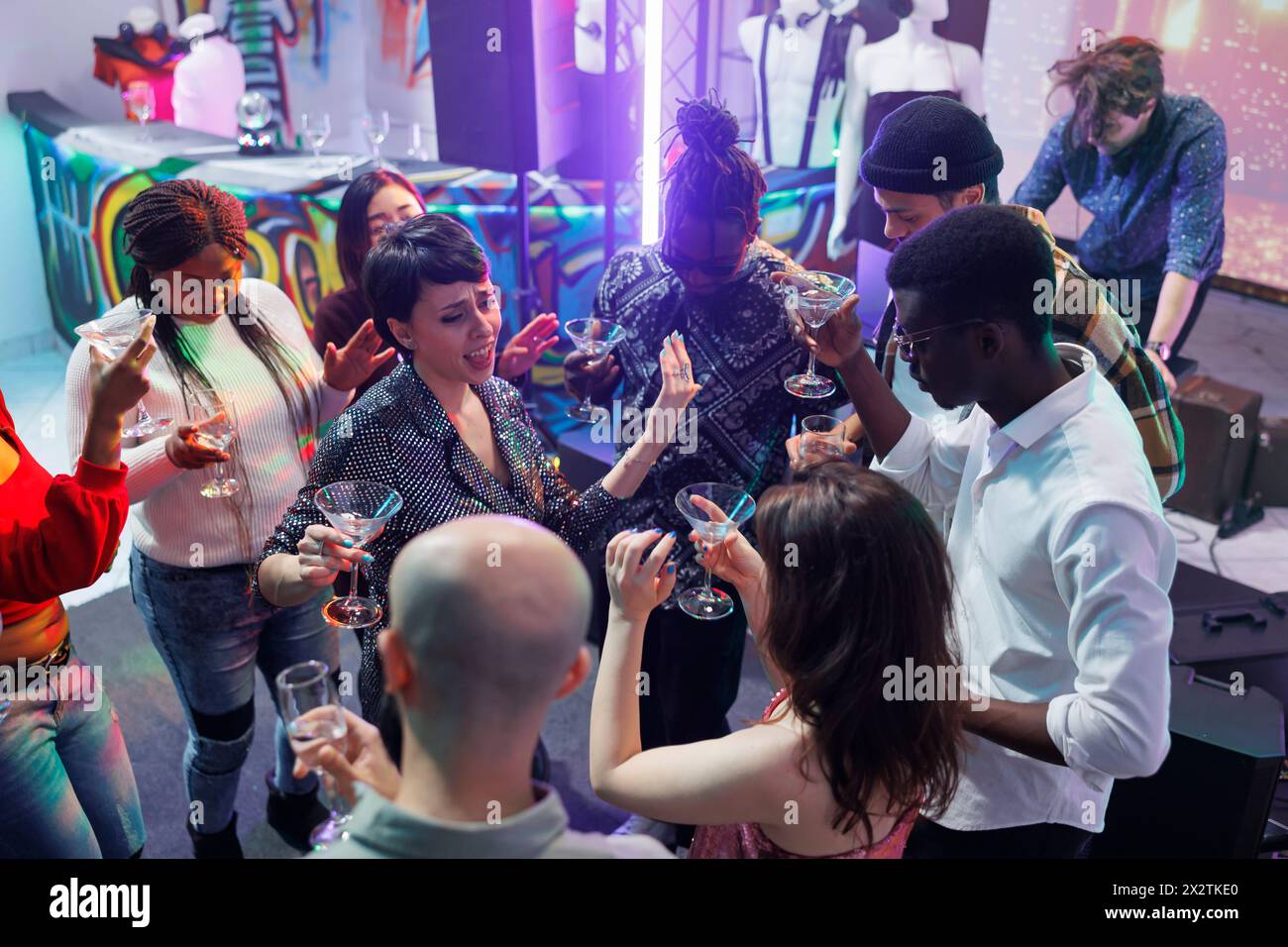 Friends drinking alcohol while dancing and singing at nightclub party. Carefree young people enjoying beverages, holding glasses and saying toast while clubbing on dancefloor Stock Photo