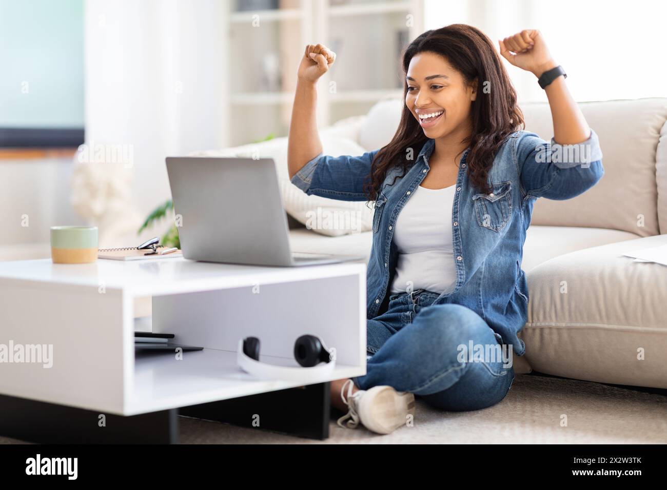 Woman Sitting on Floor in Front of Laptop, Celebrating Success Stock Photo