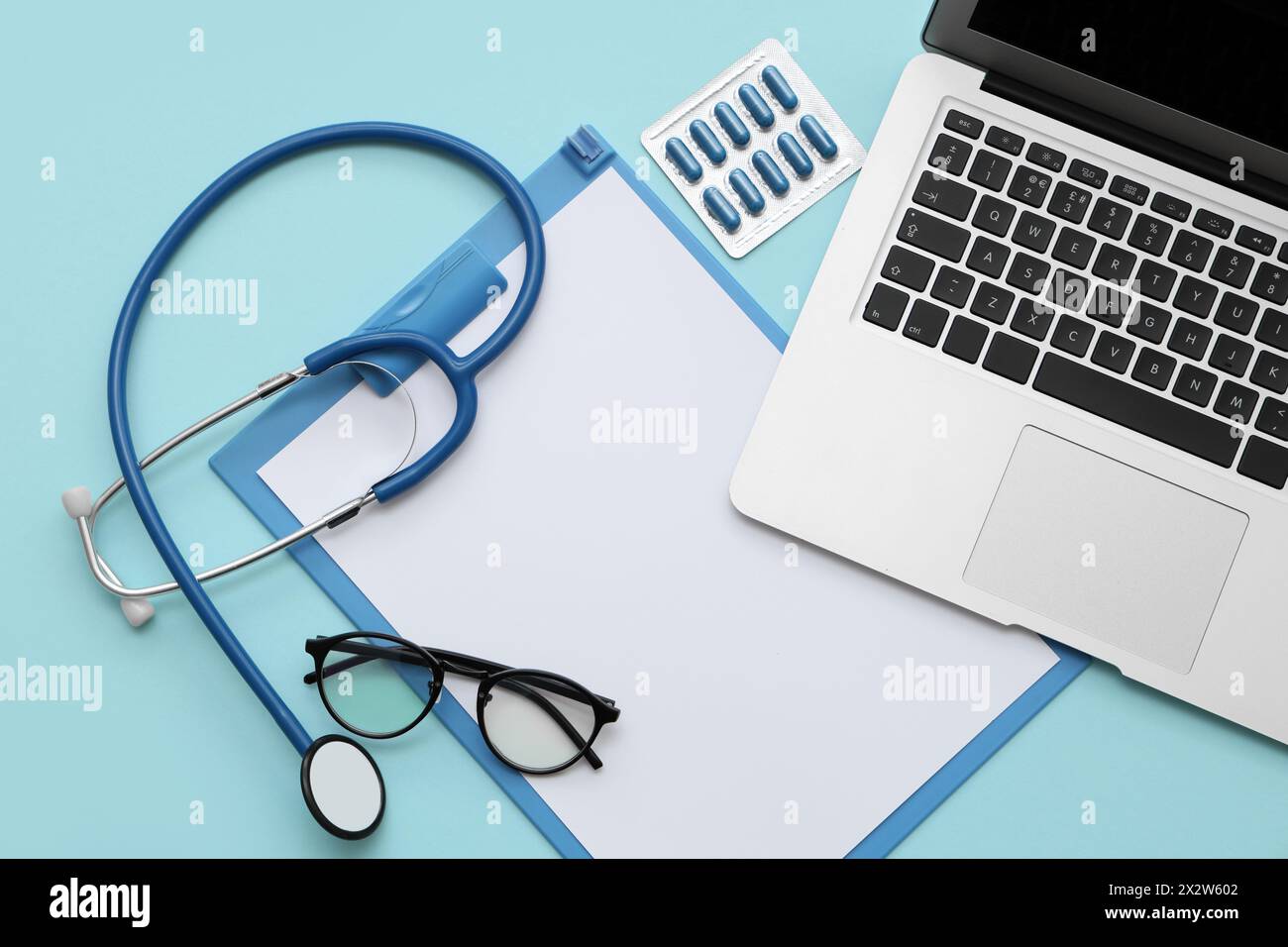 Blank clipboard with stethoscope, pills and laptop on blue background ...