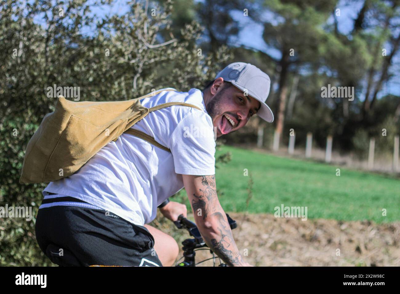 Catch a glimpse of adventure as a young male, tongue out in exhaustion, glances back while cycling through the challenges of nature, pushing his limit Stock Photo