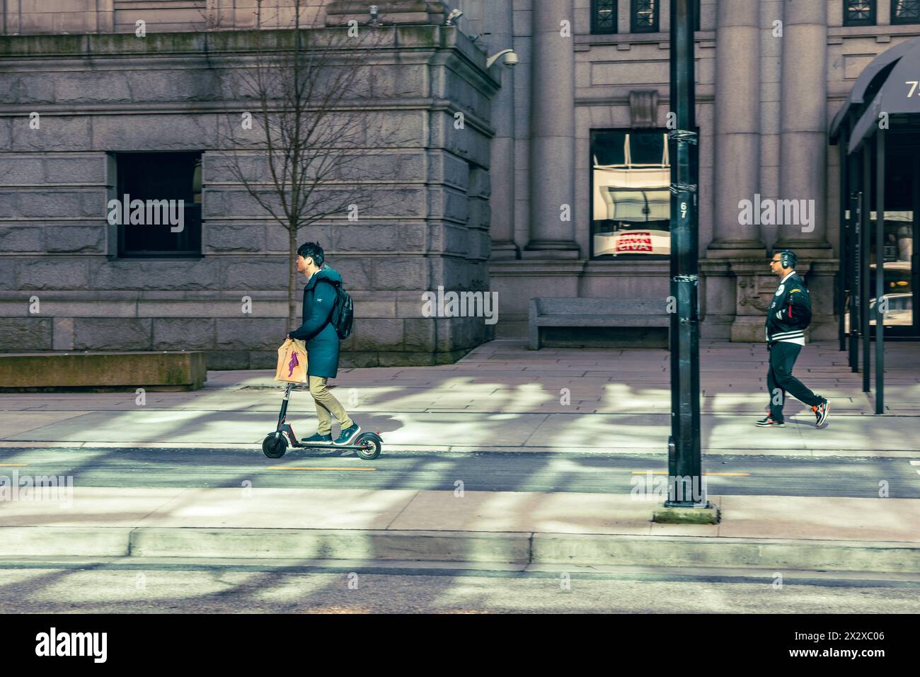 A man riding an electric scooter in the Hornby Street bike lane, in front of the Vancouver Art Gallery building illuminated by reflected light. Stock Photo