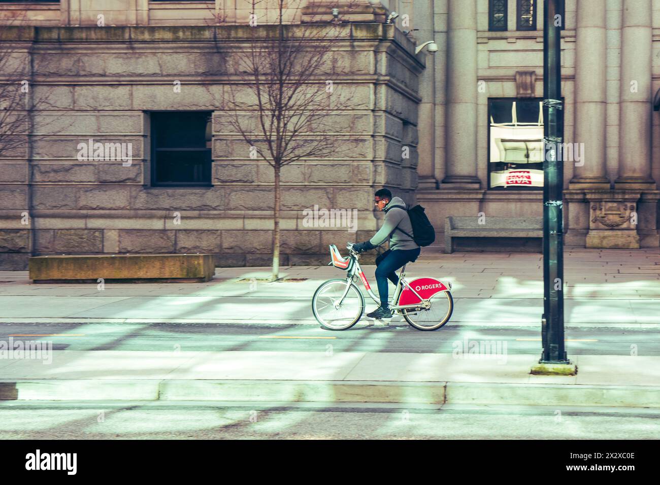 A man riding a bike share bicycle in the Hornby Street bike lane, in front of the Vancouver Art Gallery building illuminated by reflected light. Stock Photo