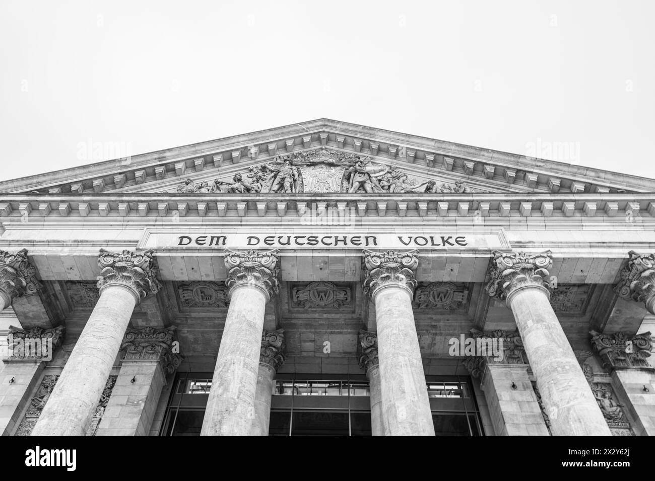 The monochrome facade of the Reichstag building, showcasing its iconic pillars and inscription: Dem Deutschen Volke. The seat of the German Bundestag, Berlin, Germany.. Black and white image. Stock Photo