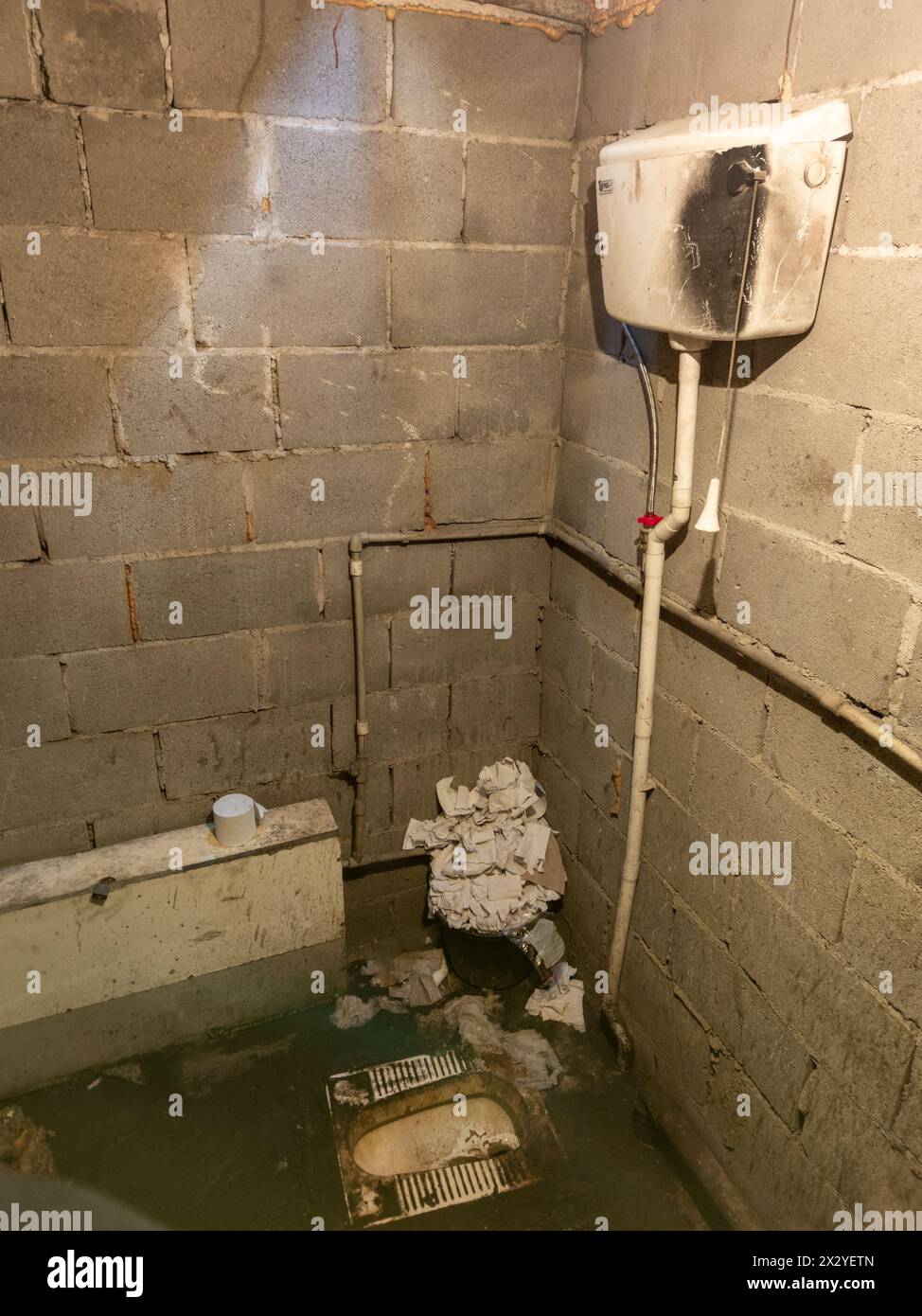 Dirty toilet room with pile of used toilet paper in the corner, uncoated concrete flooring and cinder brick walls. Stock Photo