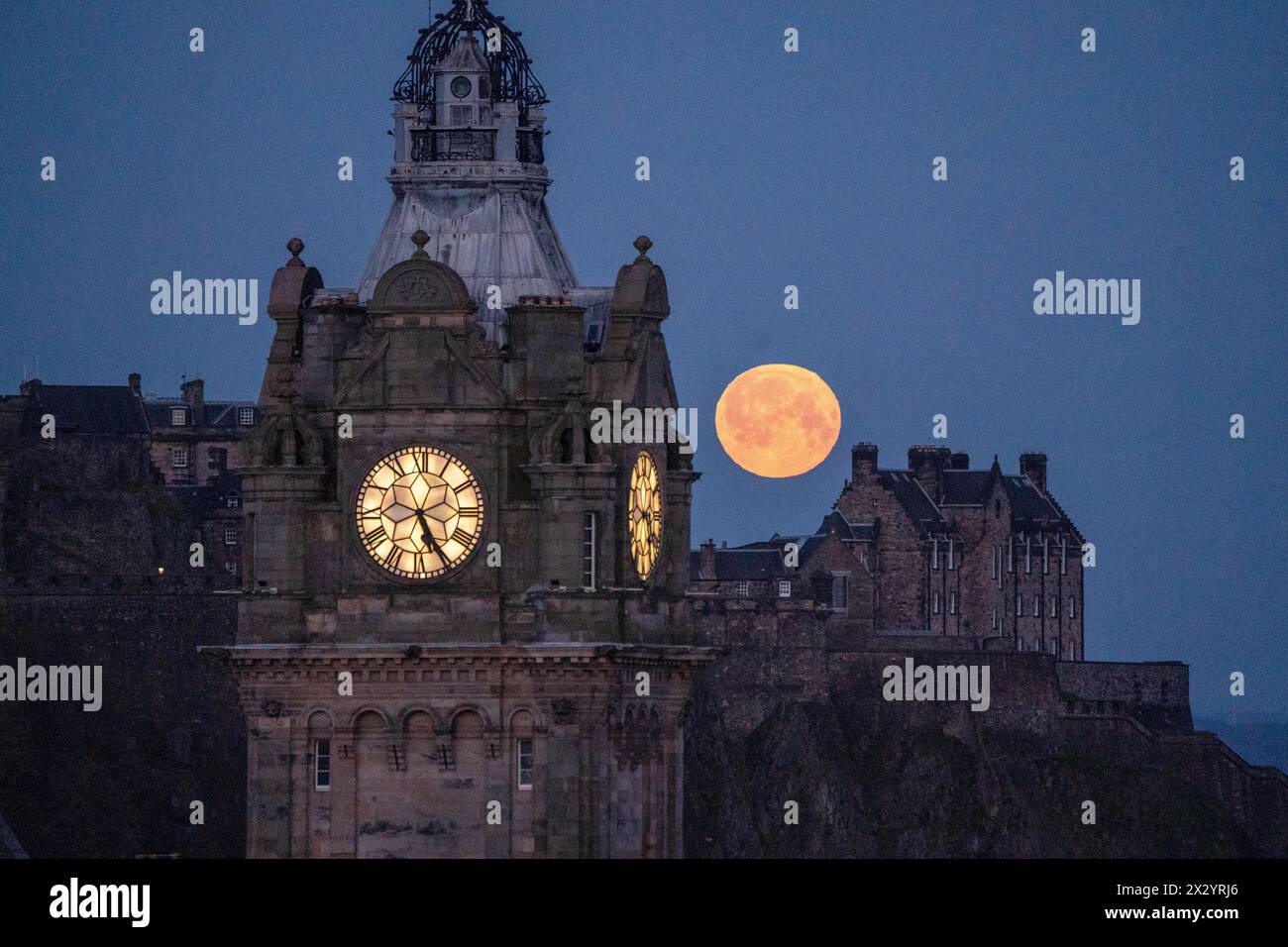 The full moon, which is known as the 'Pink Moon' during April, sets sets behind The Balmoral Clock and Edinburgh Castle. Picture date: Wednesday April 24, 2024. Stock Photo