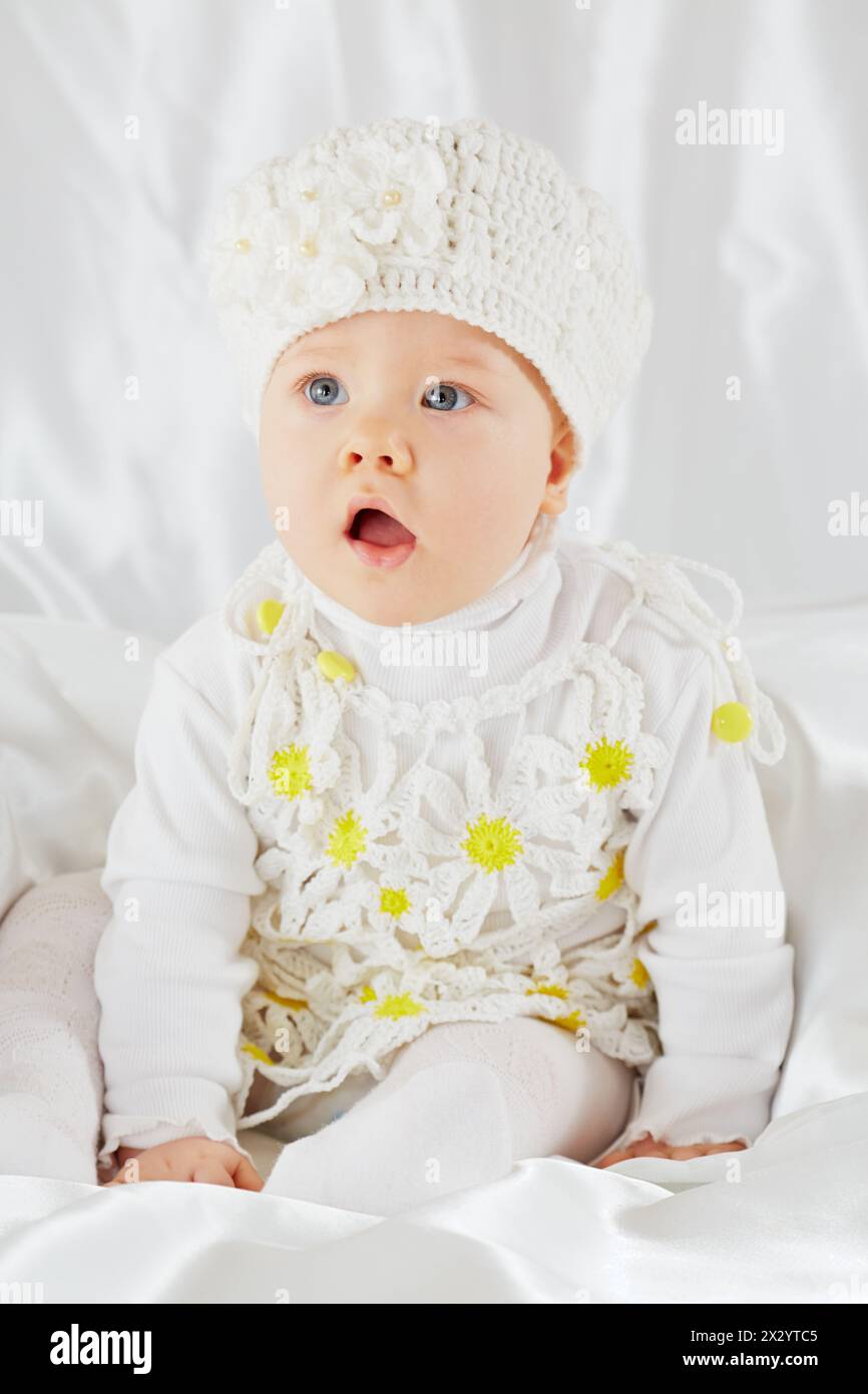 Portrait of little girl in white clothes, who sits on white coverlet Stock Photo