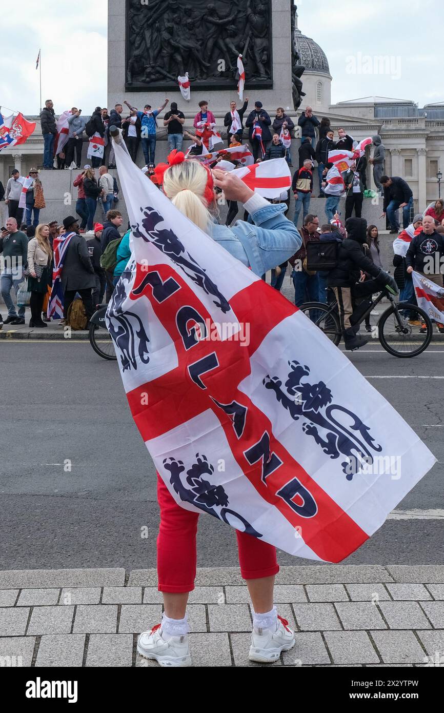 London, UK, 23rd April, 2024. Revellers stand atop the base of Nelson's Column chanting and singing football songs. A St George's Day rally, partly a celebration - and part protest, was held in Whitehall, attended by a large crowd of patriots, football supporters and others, bearing red and white flags and some in costume. Credit: Eleventh Hour Photography/Alamy Live News Stock Photo