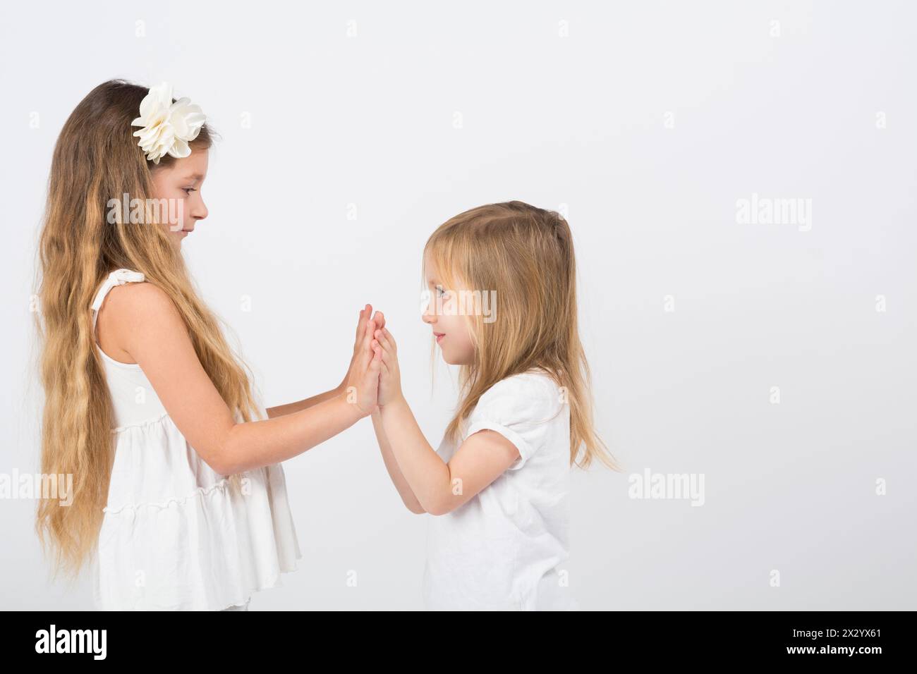 Two little girls dressed in white playing slapping each others hands Stock Photo