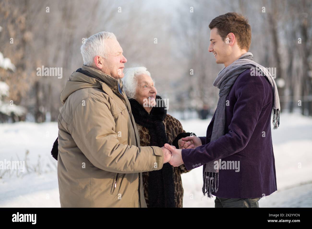 Young man wearing a scarf greets an elderly couple in the park in winter Stock Photo
