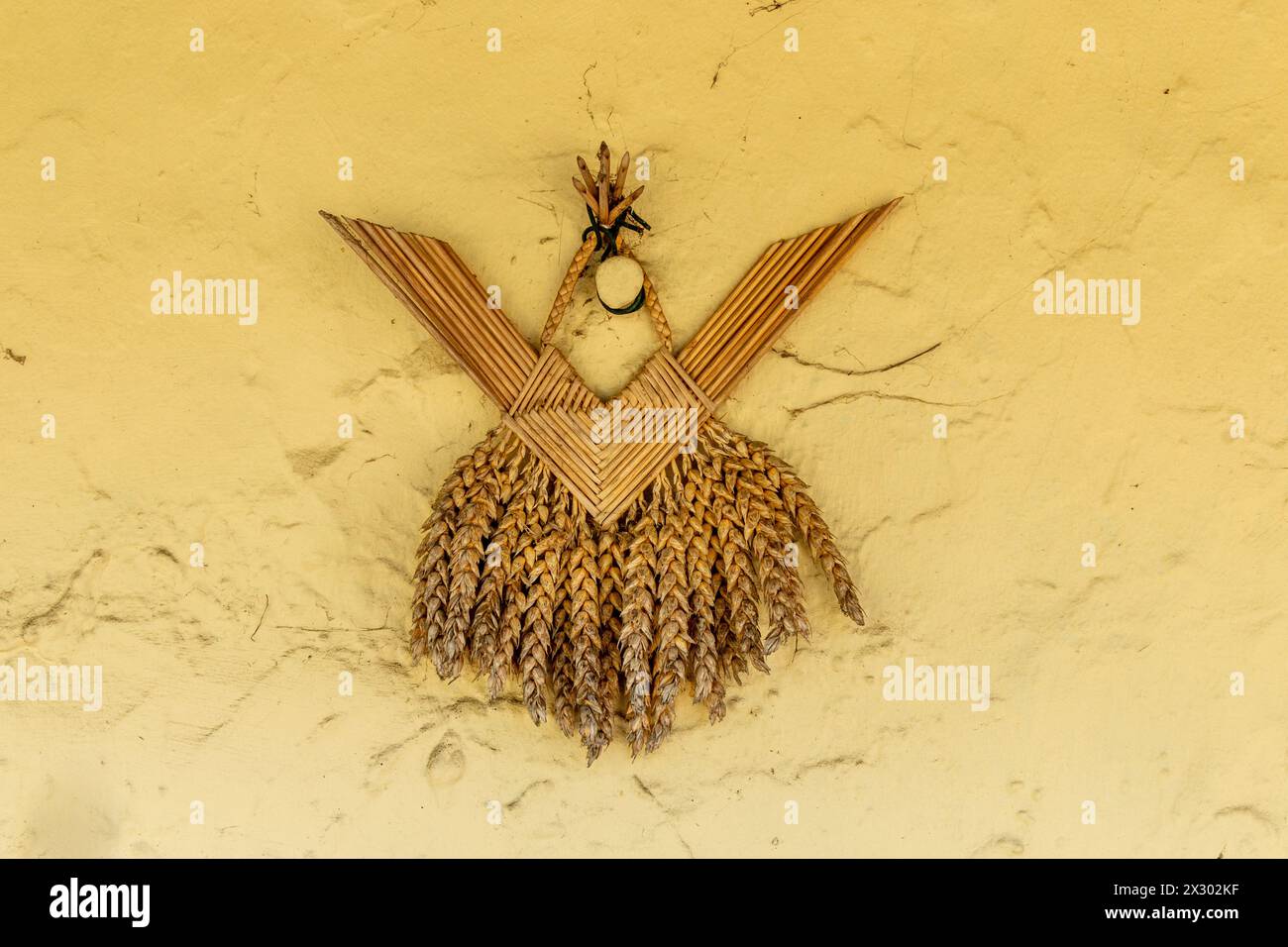 Traditional straw ornament called a corn dolly on a yellow stucco wall. Great Shelford, Cambridgeshire, England, UK Stock Photo