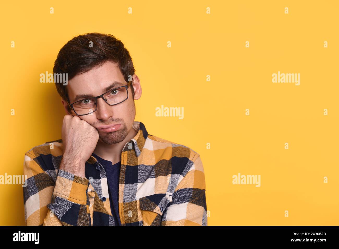 Overworked bored unhappy man looking at camera, holding hand on cheek, isolated over yellow background copy space for advertisement. Emotions and reaction, boring, dull, tedious, overwork concept Stock Photo