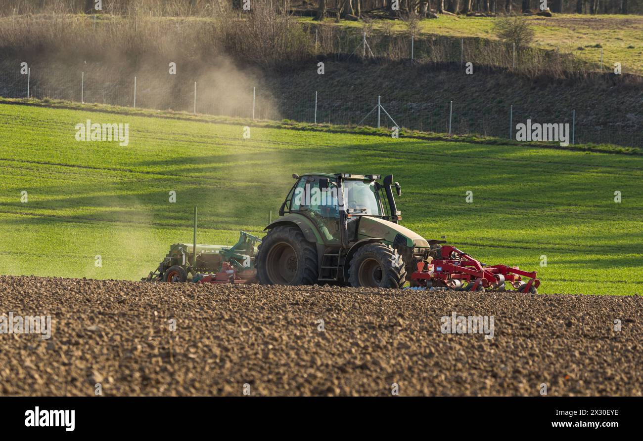 Ein Bauer ist mit seinem Traktor und der Sämaschine daran Saatgut in den Boden zu bringen. (Winkel ZH, Schweiz, 28.03.2022) Stock Photo