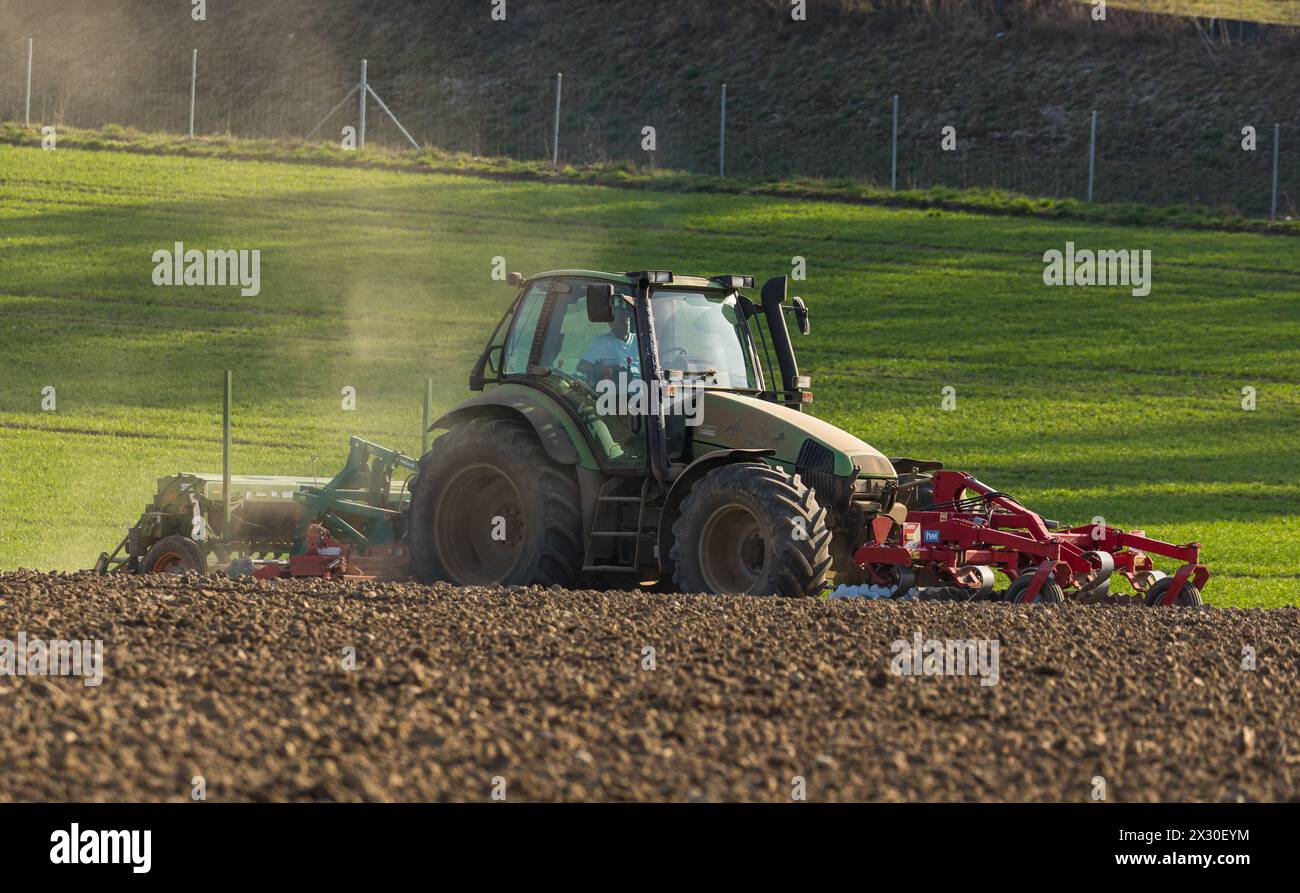 Ein Bauer ist mit seinem Traktor und der Sämaschine daran Saatgut in den Boden zu bringen. (Winkel ZH, Schweiz, 28.03.2022) Stock Photo