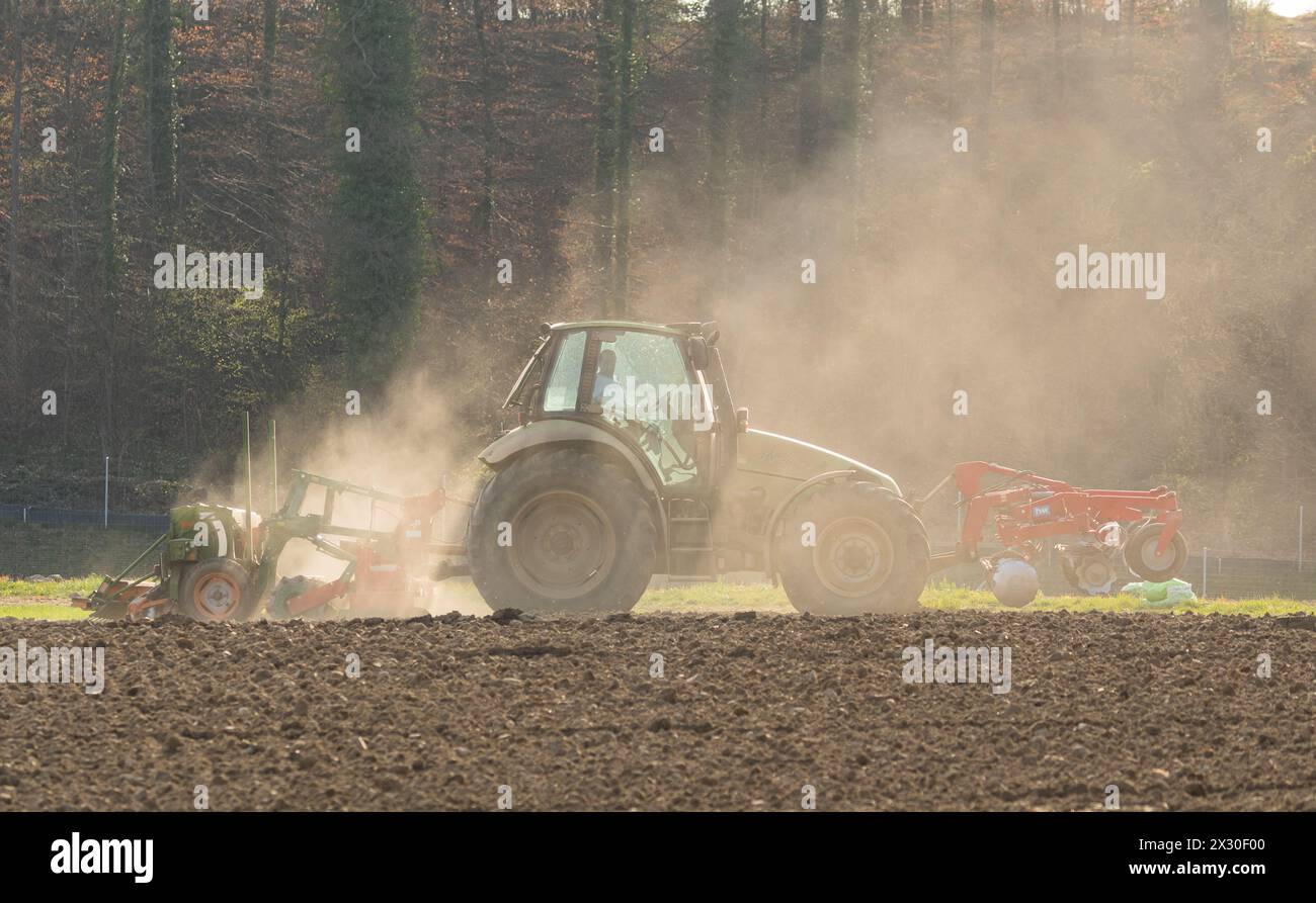 Ein Bauer ist mit seinem Traktor und der Sämaschine daran Saatgut in den Boden zu bringen. (Winkel ZH, Schweiz, 28.03.2022) Stock Photo