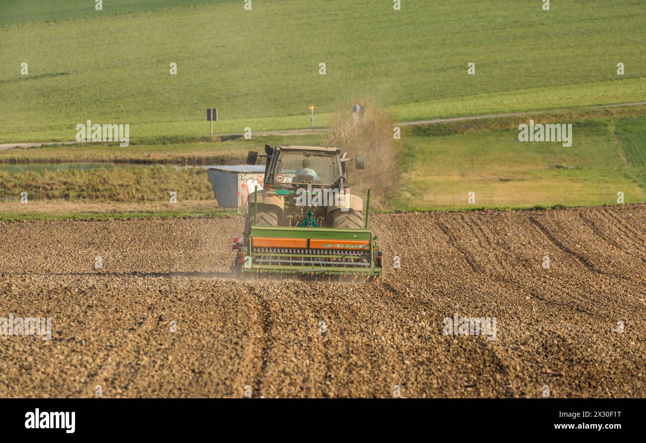 Ein Bauer ist mit seinem Traktor und der Sämaschine daran Saatgut in den Boden zu bringen. (Winkel ZH, Schweiz, 28.03.2022) Stock Photo