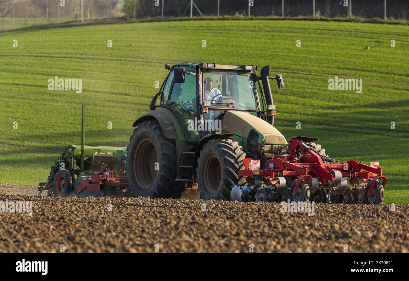Ein Bauer ist mit seinem Traktor und der Sämaschine daran Saatgut in den Boden zu bringen. (Winkel ZH, Schweiz, 28.03.2022) Stock Photo
