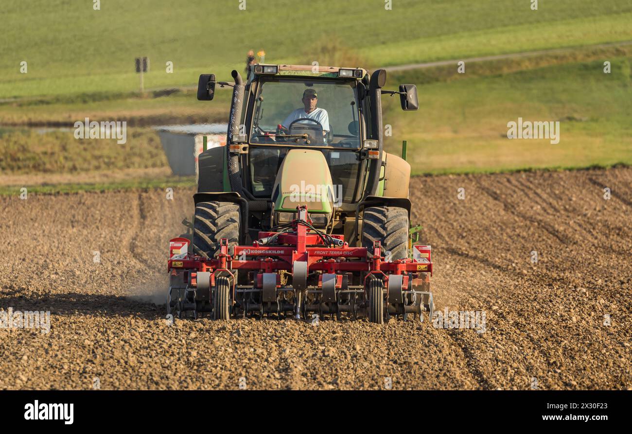 Ein Bauer ist mit seinem Traktor und der Sämaschine daran Saatgut in den Boden zu bringen. (Winkel ZH, Schweiz, 28.03.2022) Stock Photo
