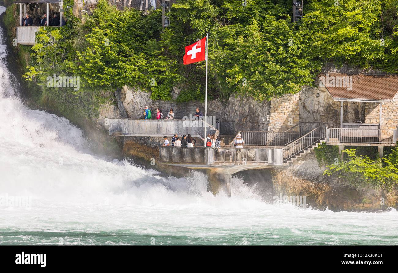 Einige Touristen beobachten die herunterstürtzenden, wilden Wassermassen des Rheinfalls auf der Zürcher Seite. (Neuhausen am Rheinfall, Schweiz, 16.05 Stock Photo