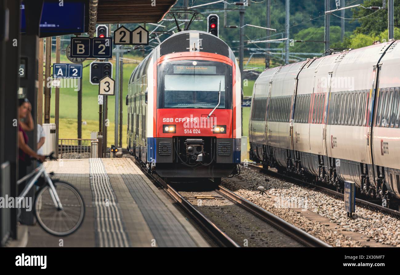 Die S-Bahn der Linie S24 fährt in den Bahnhof Bassersdorf ein. Eine Frau wartet mit ihrem Velo auf dedn Zug. (Bassersdorf, Schweiz, 06.06.2022) Stock Photo