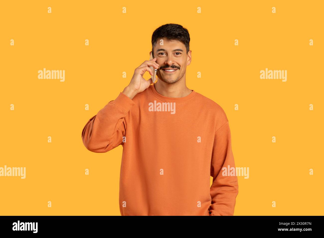 Man in Orange Sweater Talking on Cell Phone Stock Photo