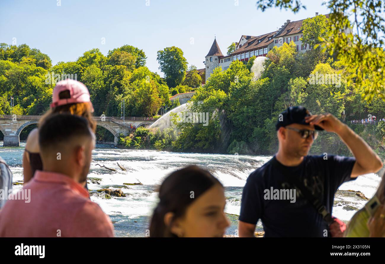 Zahlreiche Touristen bestaunen den Rheinfall. Im Hintergrund ist die Feuerwehr mit Löscharbeiten eines Flächenbrands beschäftigt.  (Neuhausen am Rhein Stock Photo