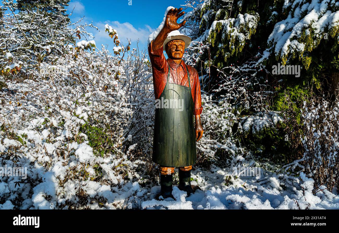 Ein aus Holz geschnitzer Mann winkt den Menschen entgegen. Auf seinem Hut und Arm ist er nach dem ersten Schneefall schneebedeckt. (Rafz, Schweiz, 11. Stock Photo