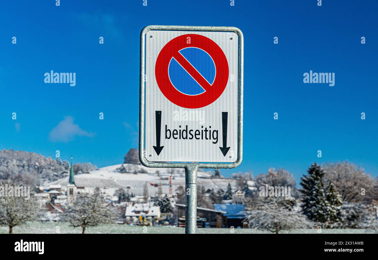Ein Verkehrsschild besagt, dass das Parkieren beidseits der Strasse verboten ist. Dahinter die Gemeinde Rafz im Zürcher Unterland. (Rafz, Schweiz, 11. Stock Photo
