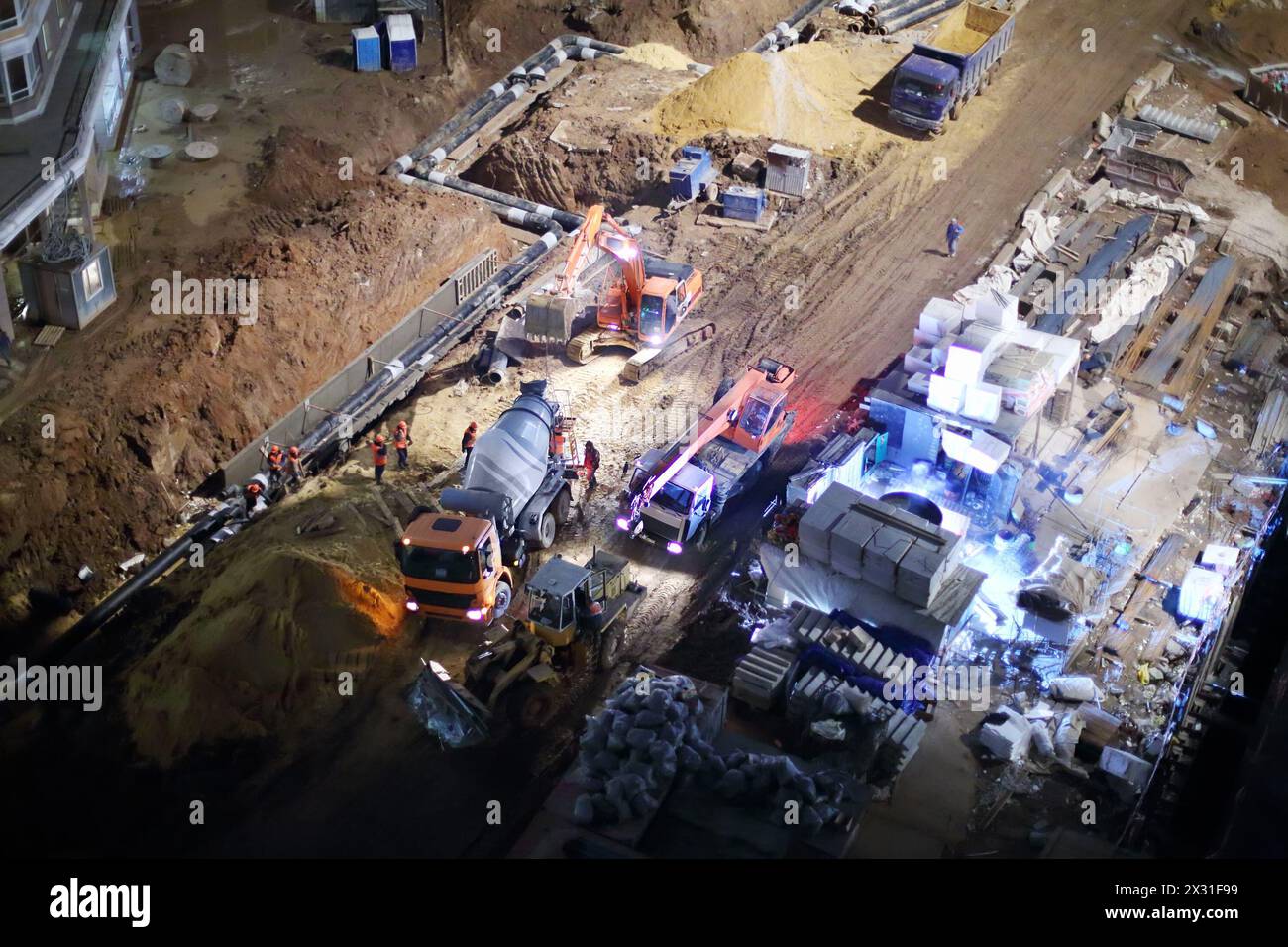 Cement mixer, crane and bulldozer at construction site at night. Stock Photo