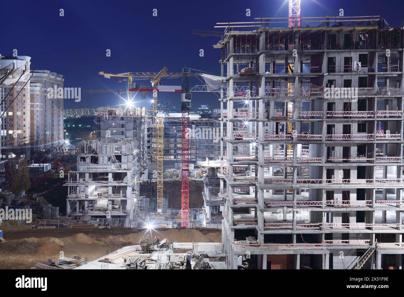 High multi-storey buildings under construction and cranes at night. Stock Photo