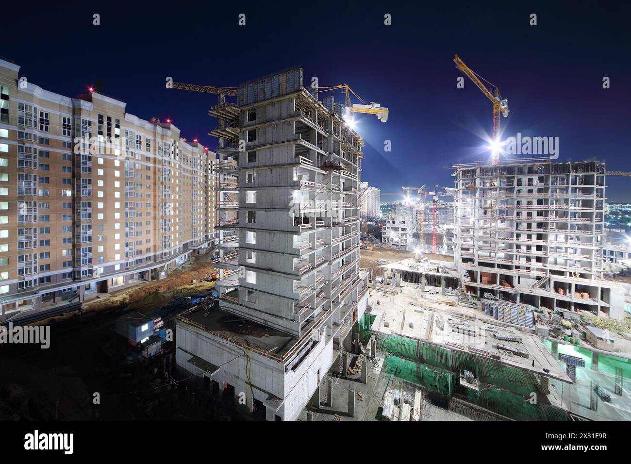 Lit high multi-storey buildings under construction and cranes at dark night. Stock Photo