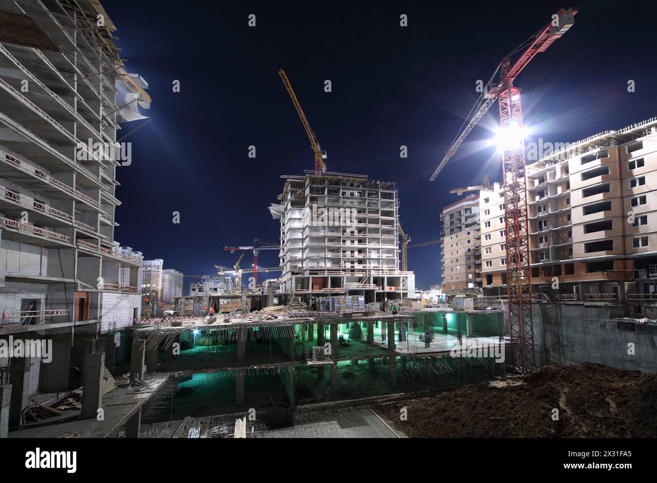 Lit multi-storey buildings under twenty-four-hour construction and cranes at night. Stock Photo