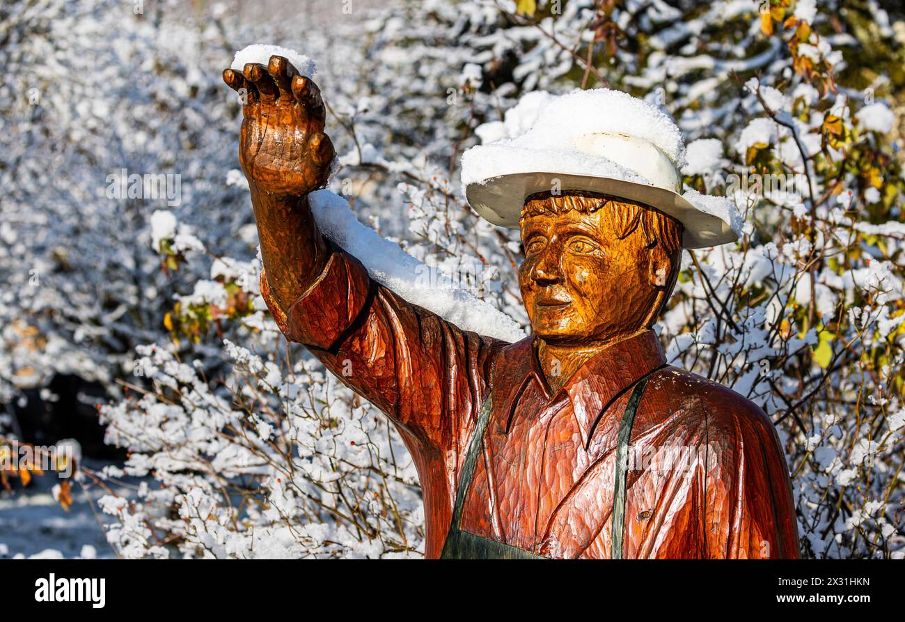 Ein aus Holz geschnitzer Mann winkt den Menschen entgegen. Auf seinem Hut und Arm ist er nach dem ersten Schneefall schneebedeckt. (Rafz, Schweiz, 11. Stock Photo