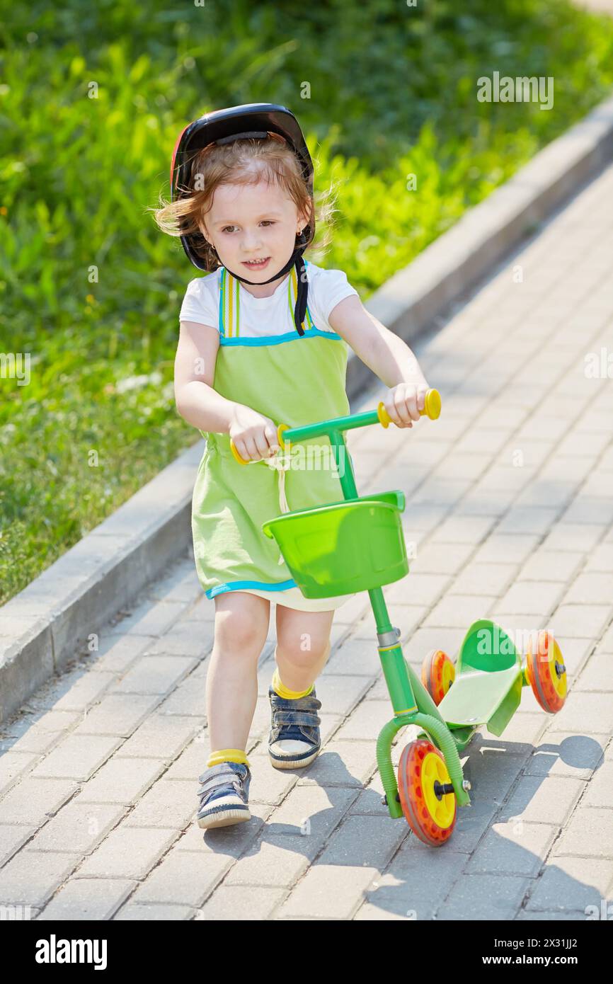 Little girl with threewheeled scooter goes along alley in park Stock