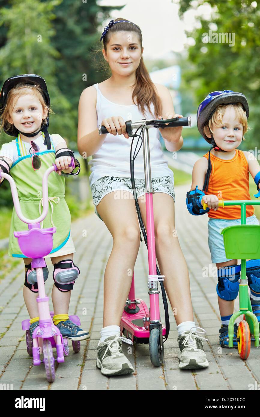 Kids Using Scooters Portrait of three children on scooters on alley at park, focus on ...