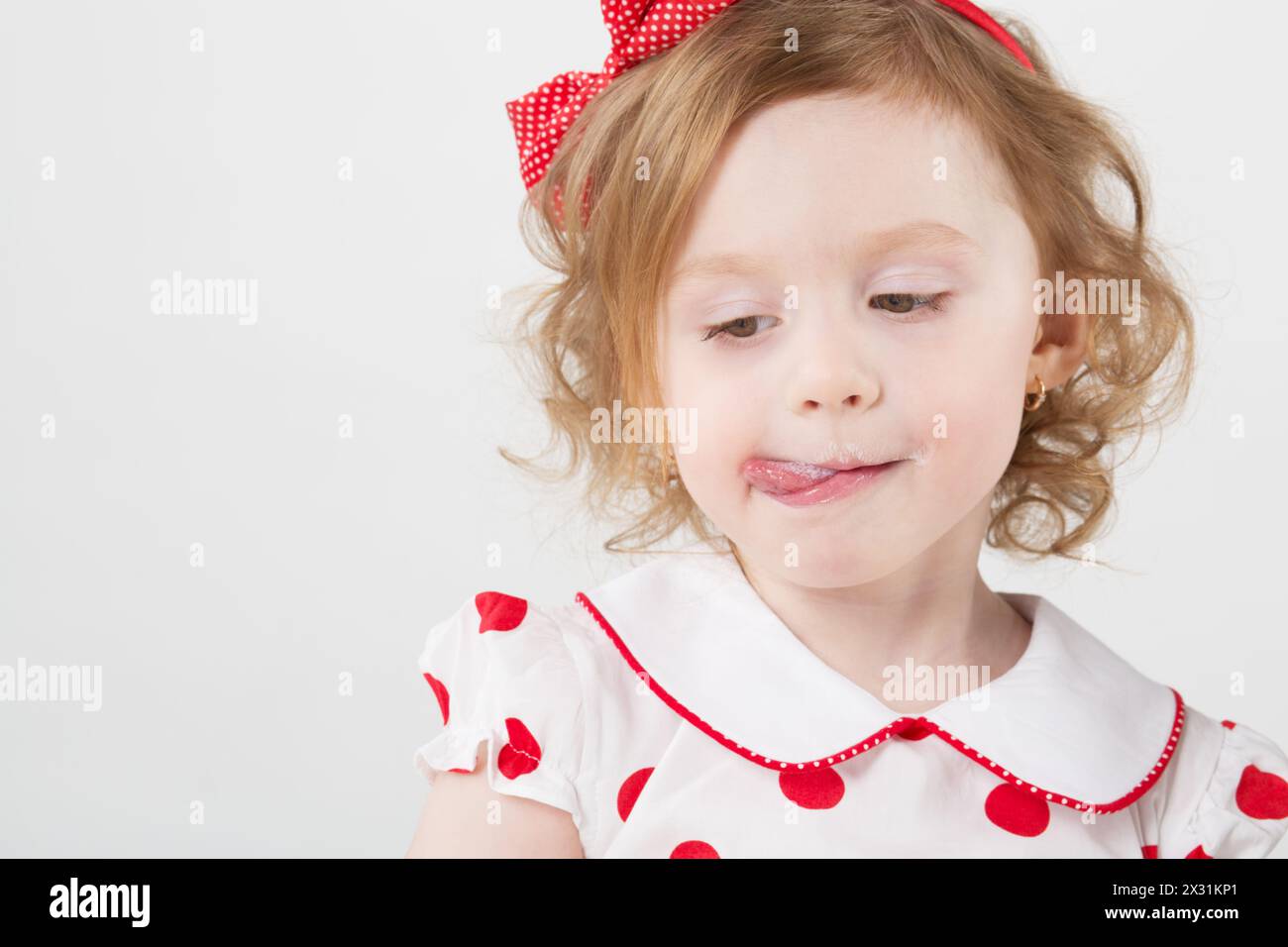 Little girl in a polka dot dress licking her lips covered with milk Stock Photo