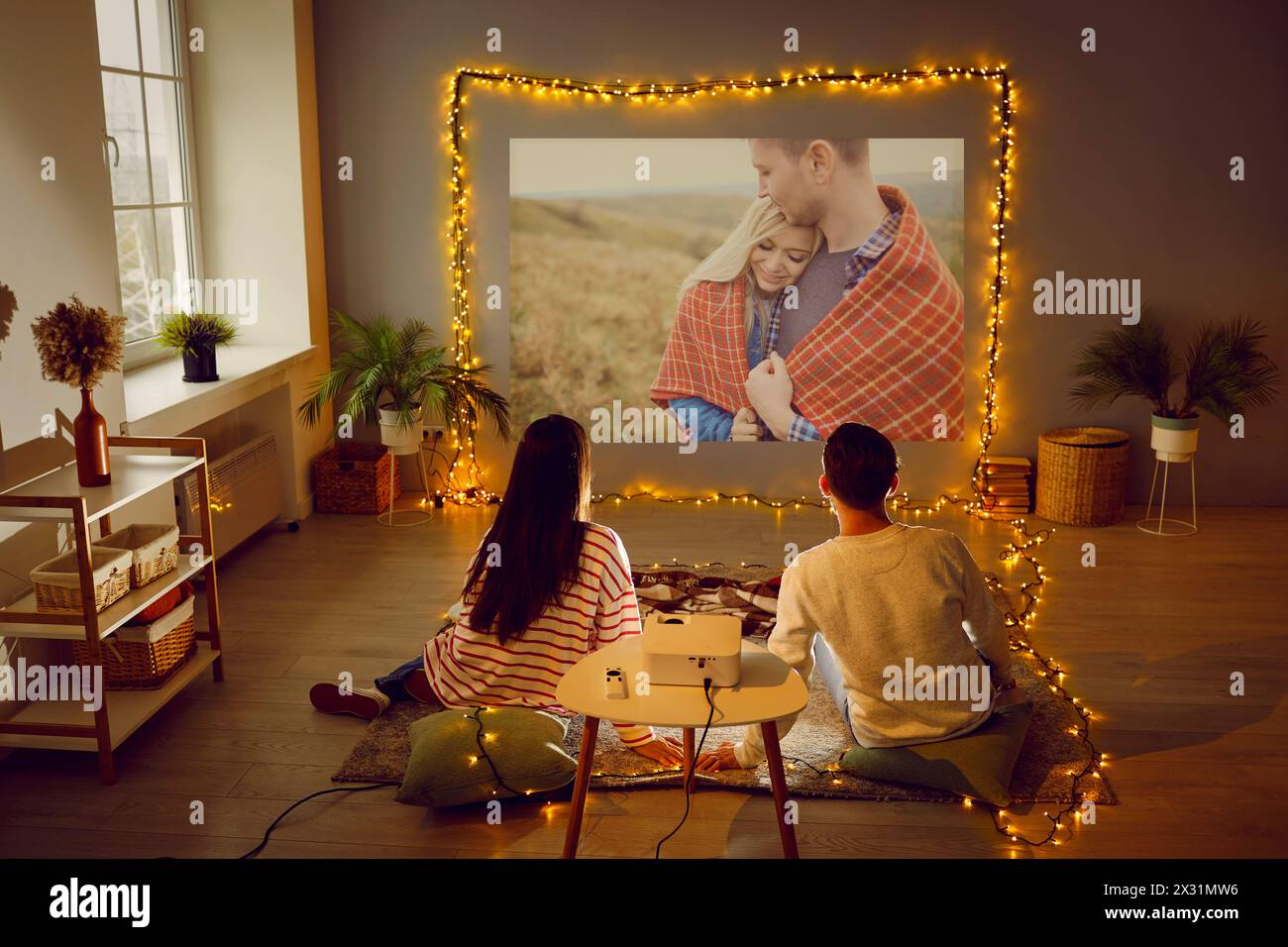 Couple enjoying Valentine's Day, having romantic date at home, watching movie on projector Stock Photo