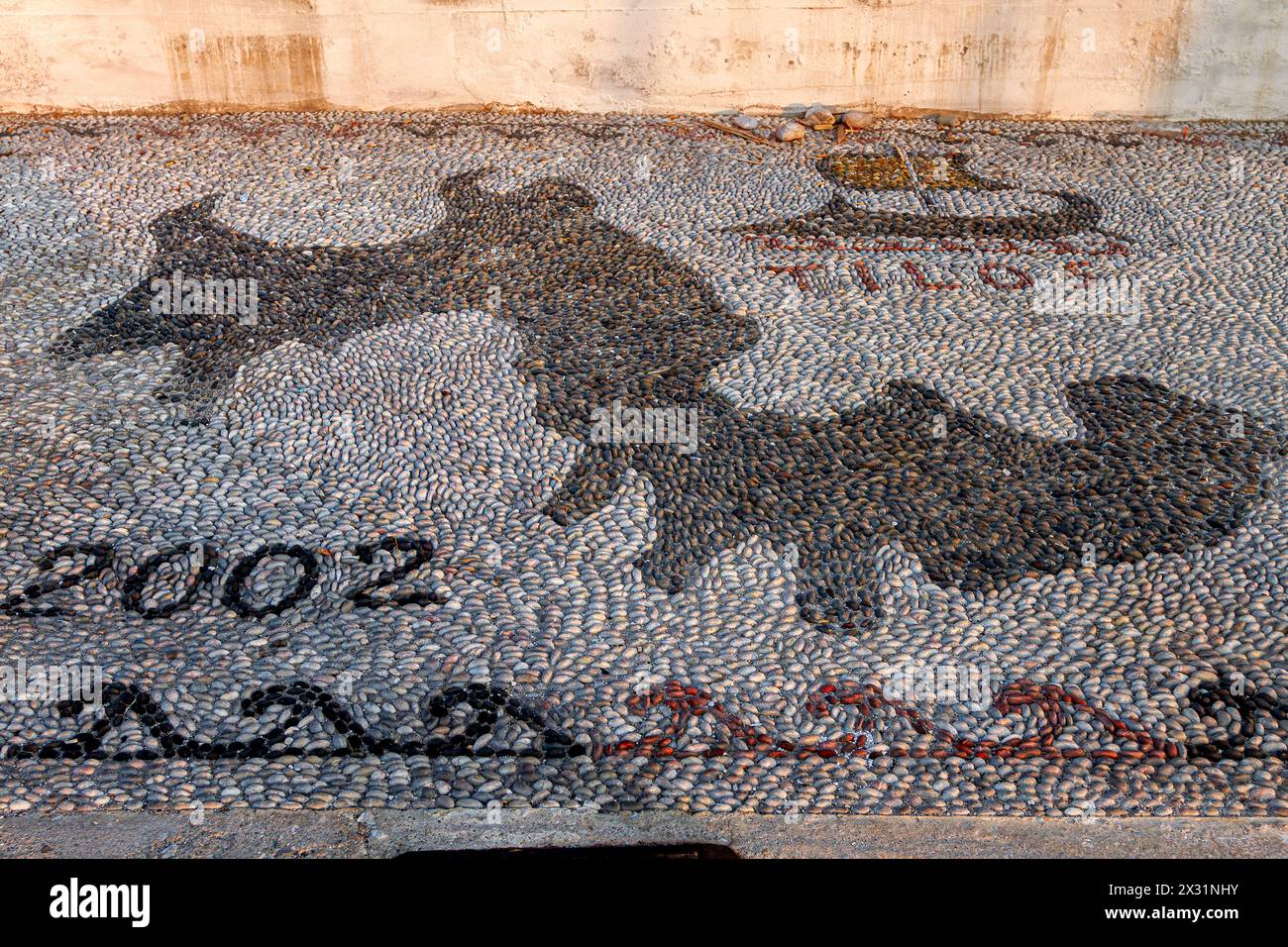 Pebble mosaic with the shape of Tilos island, the date 2002 and an ancient trireme in black pebbles, at the port of Livadia town, Tilos, Greece,Europe Stock Photo