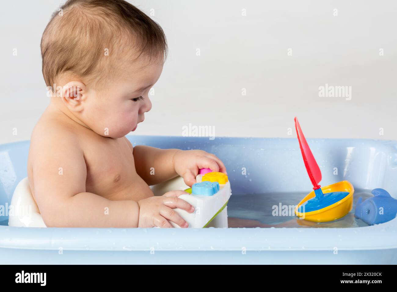 Baby boy bathes in a bathtube with toy boat Stock Photo