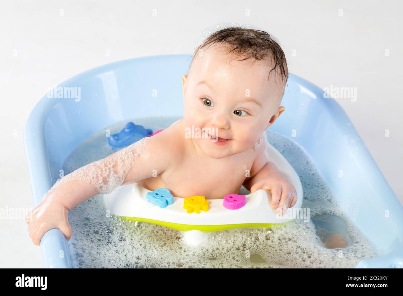 Smiling baby girl bathes in a bathtube with toys Stock Photo