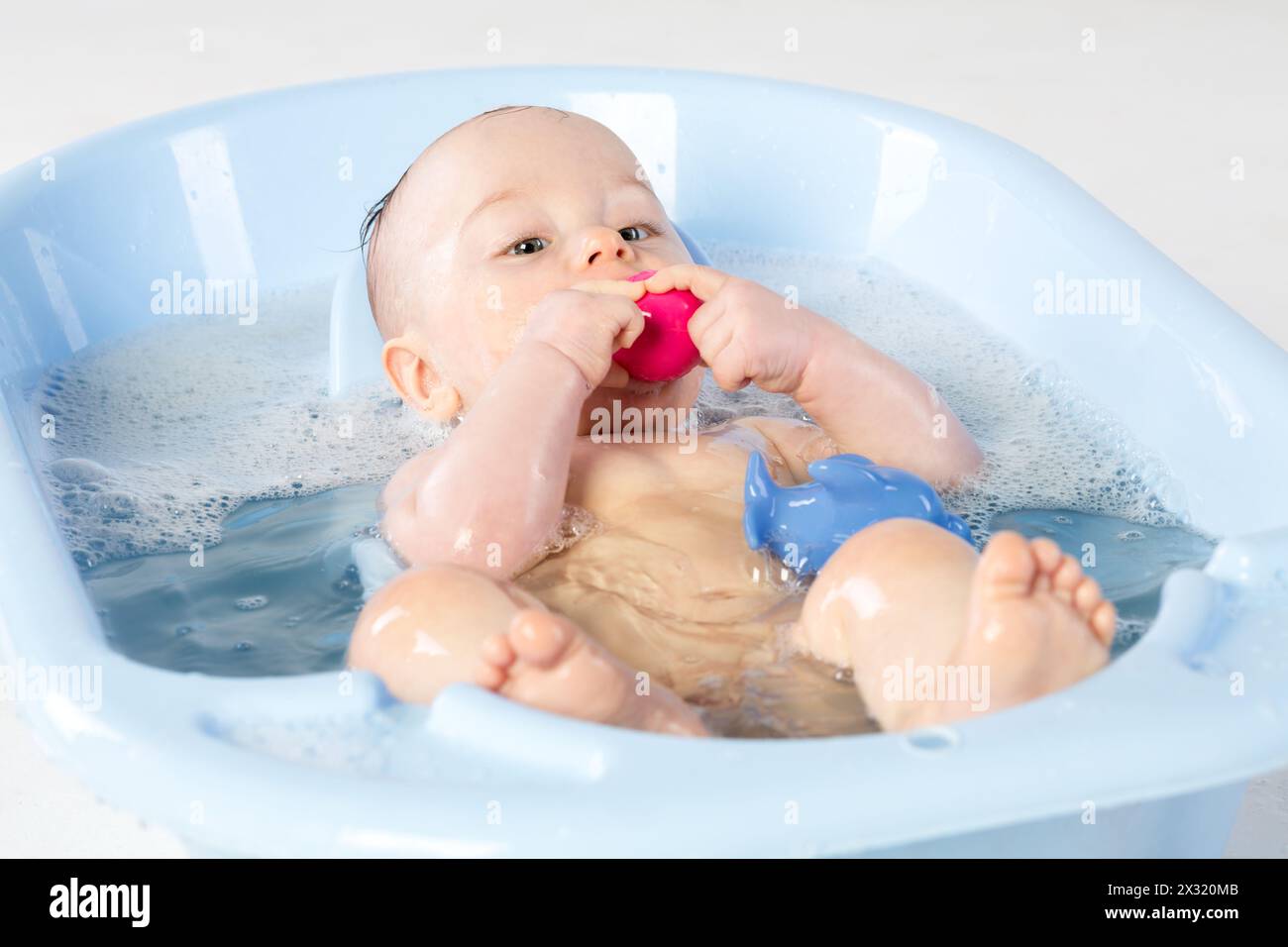 Baby girl bathes in a bathtube with toys Stock Photo