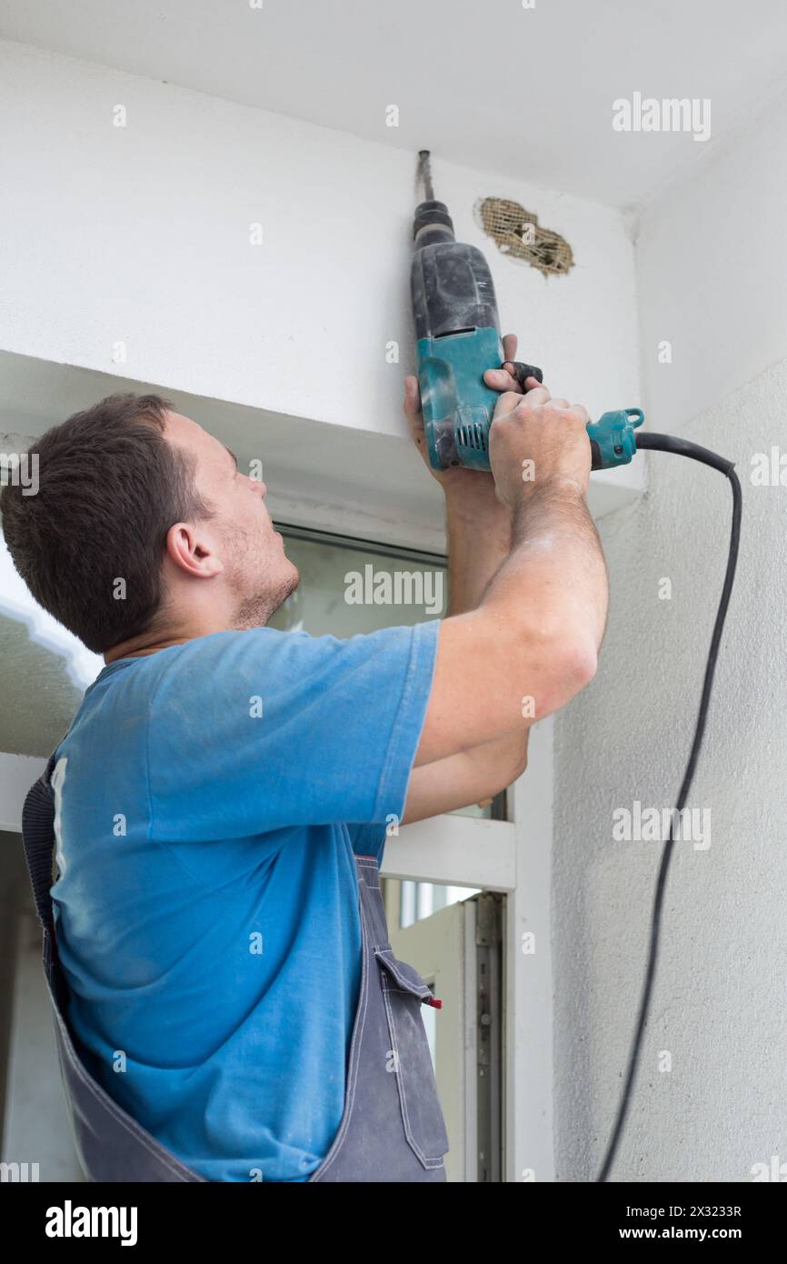 Worker makes a hole in the ceiling using a drill Stock Photo