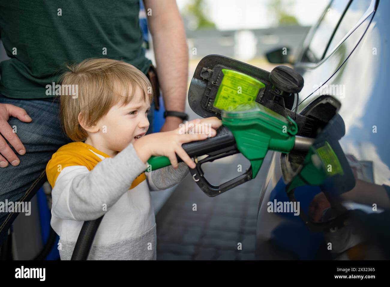 Cute little blond boy holding pump nozzle. Small funny kid helping
